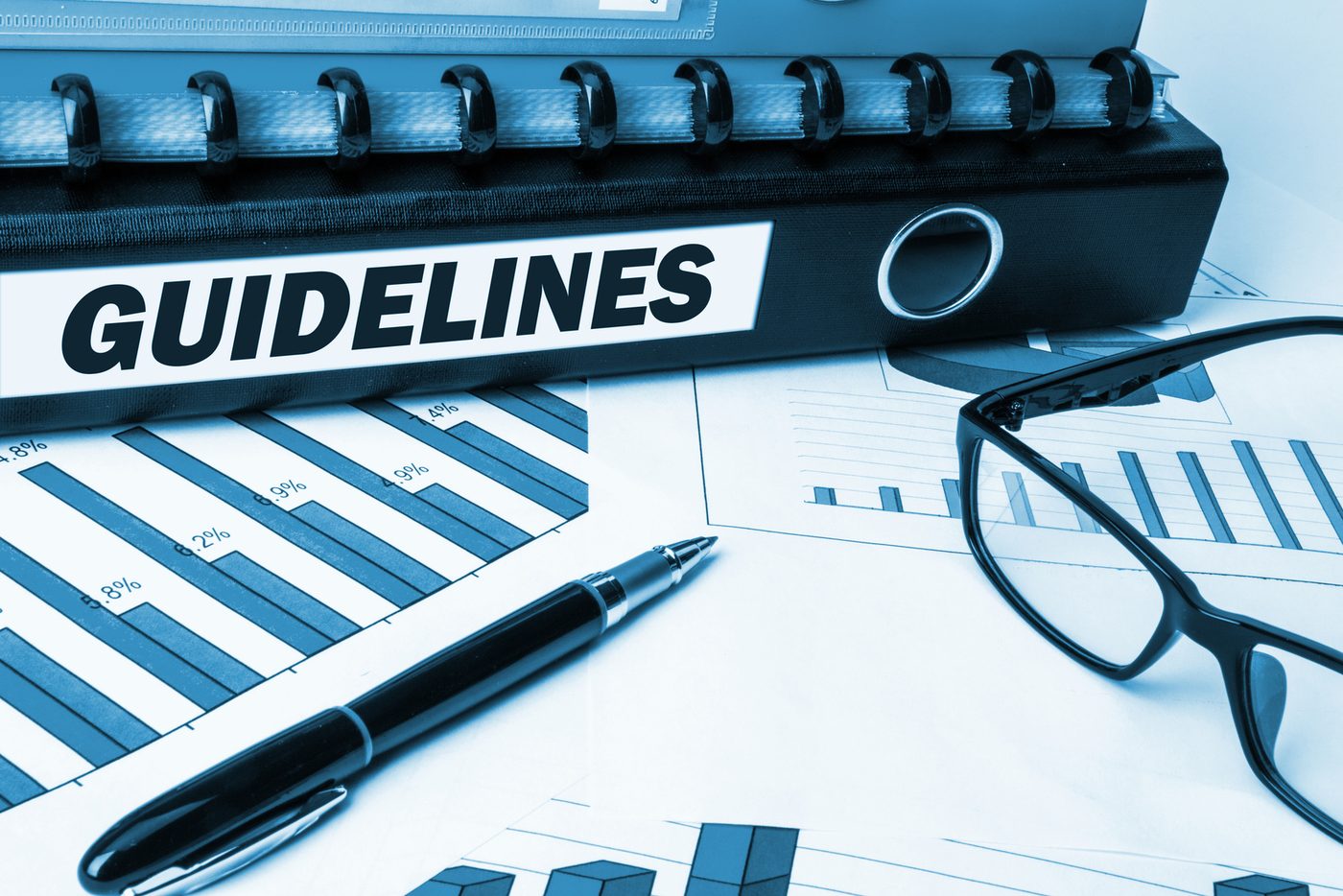 A guidelines binder beside printed charts, a pen, and glasses.